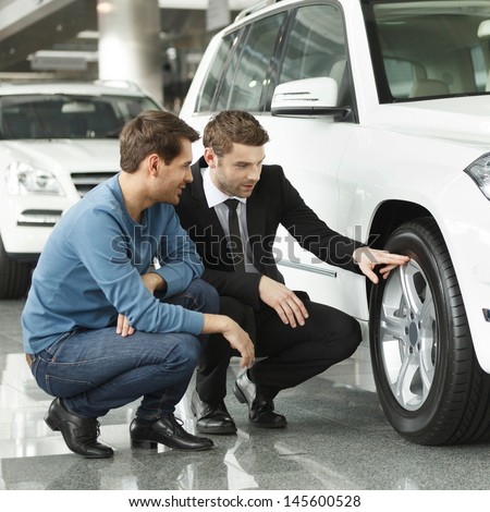 Look at these tires! Young car salesman showing the advantages of the car to the customer