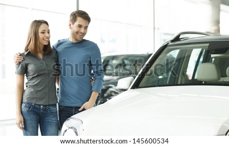 This car is exactly what we want. Beautiful young couple standing at the car dealership and making their decision