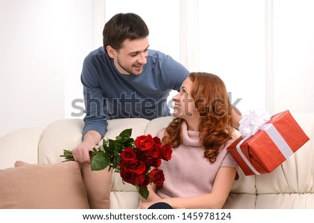 It is all for you! Handsome young men presenting a gift box and  a bunch of flowers to his attractive girlfriend
