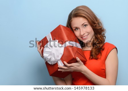 What is inside this box? Attractive young woman holding a gift box in her hands standing against blue background
