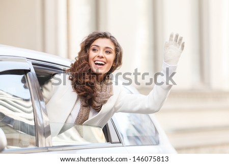 Hello! Beautiful young woman looking out from a car saying hello and waving to someone
