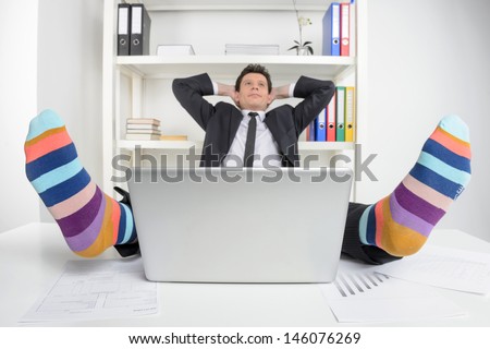 Funky socks. Happy businessman in funky socks sitting at his working place and holding head in hands