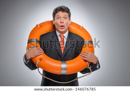 Businessman with a life buoy. Surprised businessman standing with a life buoy while isolated on gray
