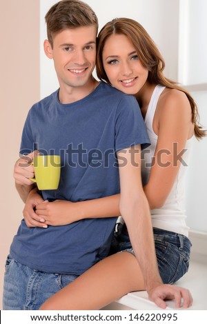Spending their free time together. Beautiful young couple standing near the window silk while men holding a cup of coffee