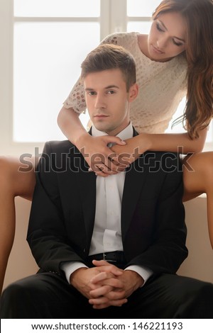 Couple in style. Beautiful young couple sitting close to each other while men in formal wear looking at camera