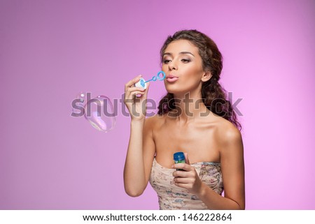 Beauty with bubble wand. Beautiful young women blowing into the bubble wand while standing isolated on colored background