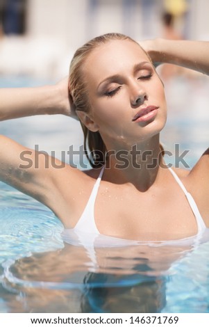 Hot summer day. Attractive young women in bikini relaxing in pool with her eyes closed