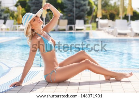 Having a good time on the poolside. Side view of attractive young women in bikini posing on the poolside