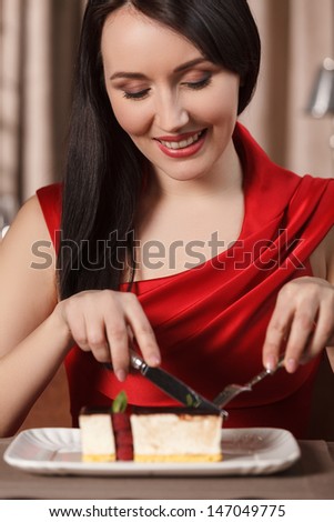 Tasty cake. Beautiful women in red dress eating cake at the restaurant