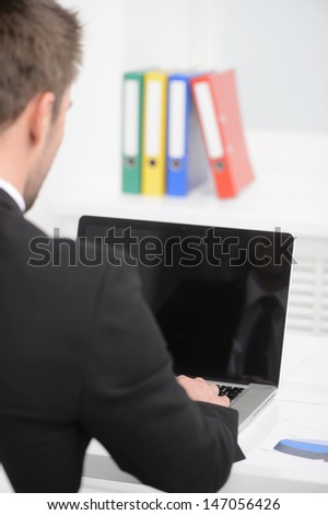 Working on the computer. Rear view of businessman in formalwear working on the laptop while sitting at his working place