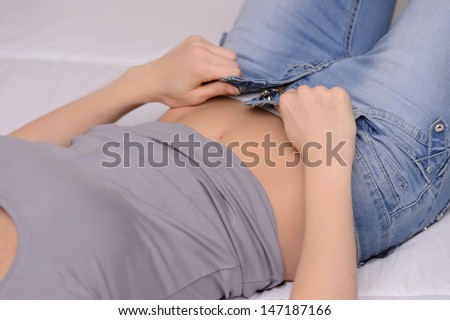 Dressing the new jeans. Cropped image of women trying to dress her jeans while lying on the sofa