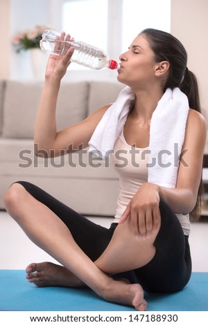 Feeling thirsty. Tired young women in sports clothing drinking water while sitting on the exercise mat