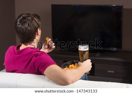 Young men watching TV. Rear view of young men drinking beer and eating snacks while watching TV