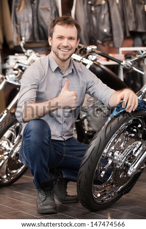 Happy motorcycle owner. Cheerful young men crouching near his new motorcycle
