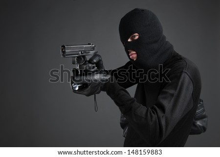 Criminal. Side view of men in black balaclava aiming with a gun and flashlight while standing isolated on black