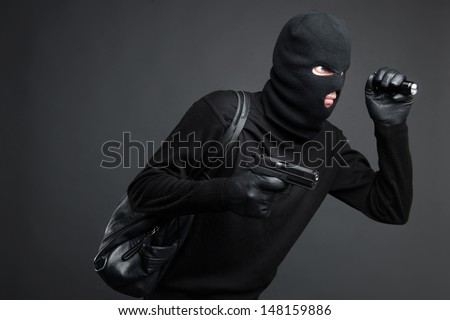 Thief. Side view of men in black balaclava holding a gun and flashlight while standing isolated on black