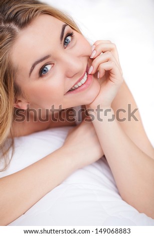 Beauty in bed. Top view of beautiful young women lying on bed and holding her hand on chin