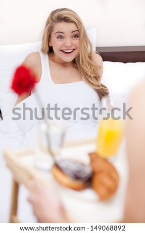Breakfast in bed. Surprised young women lying in bed while her boyfriend serving breakfast in bed
