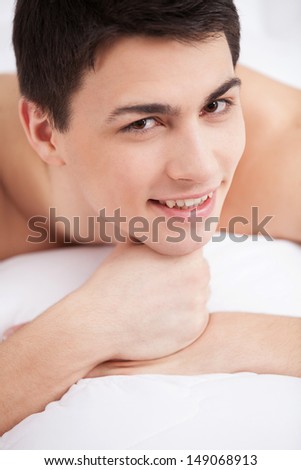 Man in bed. Handsome young man lying on bed and smiling