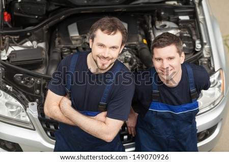 Confident mechanics. Top view of two cheerful auto mechanics looking at camera and smiling