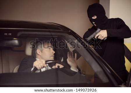 Where is the money? Men in black balaclava holding gun and aiming a shocked mature businessman sitting on the front seat of a car