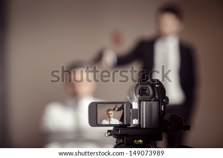Crime scene.  Close-up of home video camera shooting a man in formalwear aiming a tied-up businessman