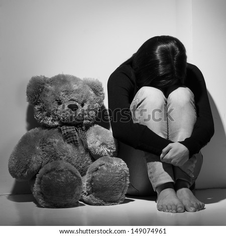Depressed women. Black and white image of young depressed women sitting on the floor near teddy bear and hiding her face behind knees