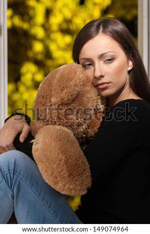 Women with teddy bear. Depressed young women sitting in front of the window and hugging her teddy bear
