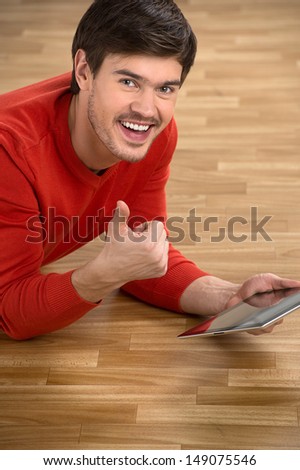 Men with digital tablet. Top view of cheerful young men gesturing while lying on the floor with a digital tablet in his hand