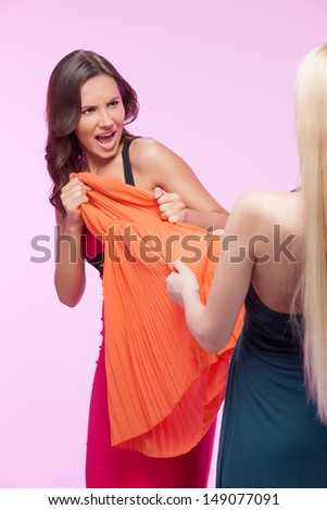 This dress is mine! ItÃ?Â¯Ã?Â¿Ã?Â½ mine! Two angry young women trying to take away one dress while isolated on pink background