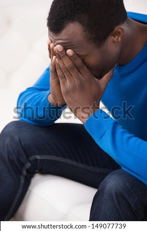 Depressed men. Top view of sad African descent men sitting on the couch and covering his face with hands