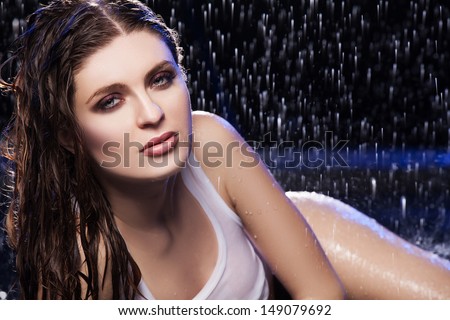Wet beauty. Beautiful young women looking at camera while lying on the floor under the rain