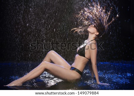 Wet women. Beautiful wet women in black bikini sitting on the floor under the rain