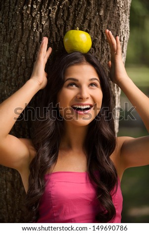 Apple on her head. Beautiful young woman standing back to the tree and holding apple on her head