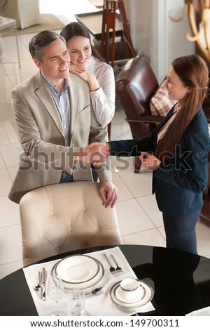 Making a deal. Cheerful middle-aged couple standing in furniture store while man shaking hand to sales clerk