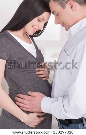 Waiting for baby. Happy man touching his pregnant wife belly and smiling