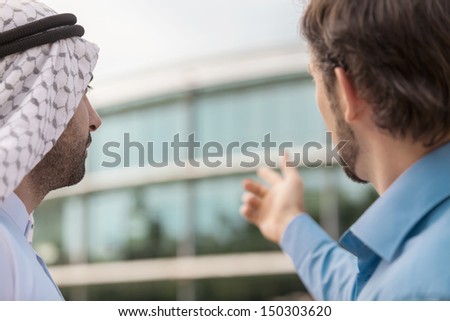 Discussing business issues. Rear view of two business partners discussing something while one of them pointing the building