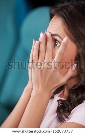 Watching  horror movie. Side view of terrified young women covering her face with hand while watching movie at the cinema