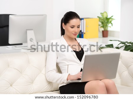 Working at the computer. Beautiful middle-aged businesswoman sitting on the couch and typing something on the computer