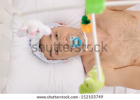 Big baby. Top view of infant adult man with pacifier looking at camera while lying on the baby bed
