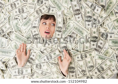 Rich woman. Top view of surprised young woman covered with US paper currency