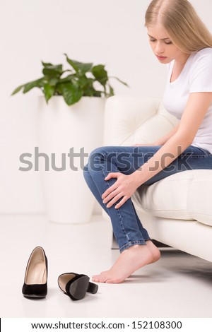 Tired woman. Side view of tired young woman sitting on the couch and touching leg