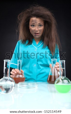 Experiment failed. Frustrated young woman in lab coat holding laboratory glasses and looking at camera while isolated on black