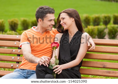 Loving couple on the bench. Cheerful young couple sitting close to each other on the bench and looking at each other