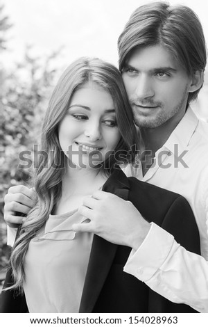 Beautiful couple. Black and white image of beautiful young couple standing close to each other while man covering woman with his suit