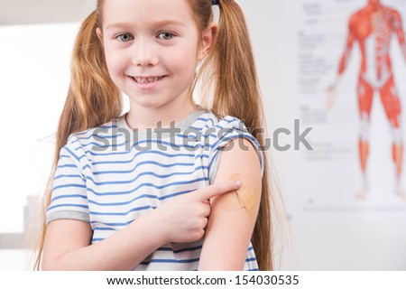 Vaccination. Cheerful little girl holding finger on the arm and smiling