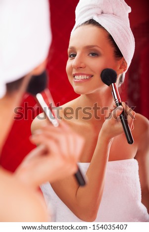 Morning make-up. Beautiful young woman covered with towel doing her make-up and smiling