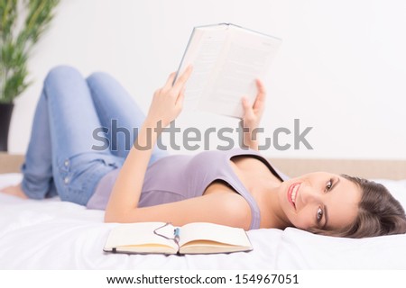 Woman reading. Cheerful young woman reading book while lying on the sofa