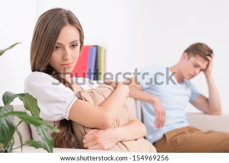 Relationship difficulties. Sad young couple sitting on the couch and looking away