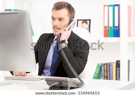 Businessman at work. Confident young man in formalwear working at the computer and talking on the phone